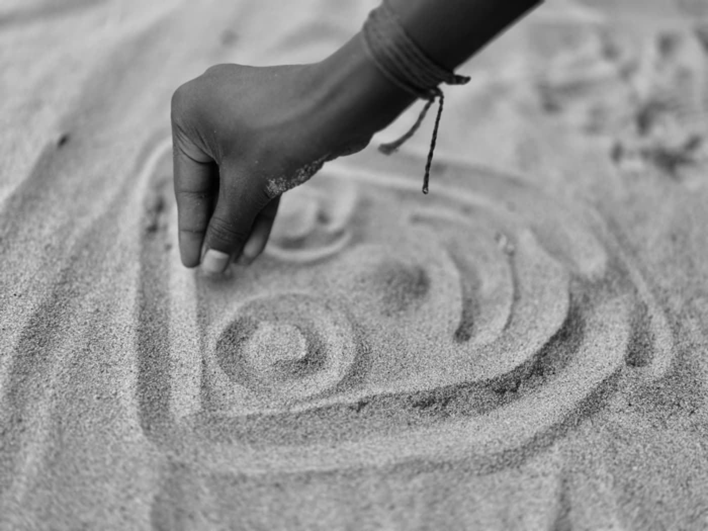 A hand drawing calming shapes in sand
